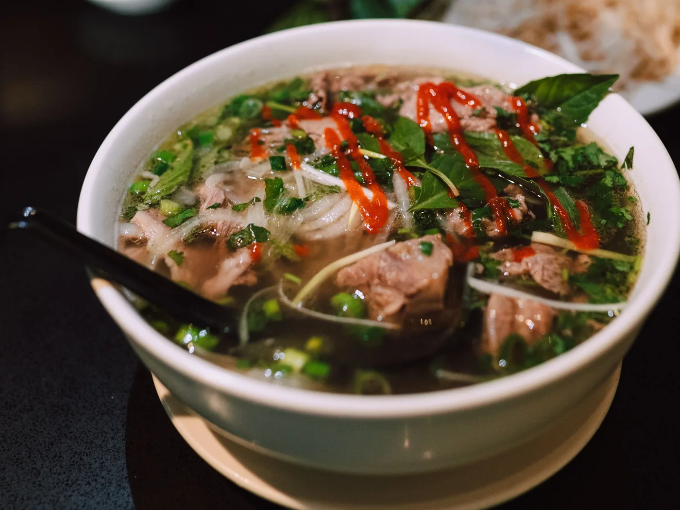 A steaming bowl of Vietnamese pho noodle soup with herbs
